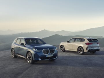 Deux SUV BMW X3, un modèle 2024, sont garés au coucher du soleil sur un terrain plat avec un arrière-plan montagneux ; l'un est bleu et l'autre est blanc. Ils sont équipés d'un moteur à essence et d'un moteur diesel.