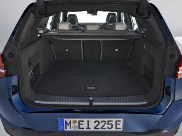 Le coffre ouvert d'une BMW X3 bleue de 2024 montre un espace de chargement vide et spacieux avec les sièges arrière rabattus. La plaque d'immatriculation indique 
