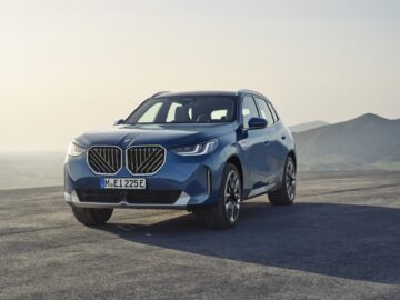 Un SUV électrique BMW iX1 bleu est garé sur une route ouverte avec des montagnes au loin et un ciel brumeux en arrière-plan, offrant un aperçu de ce que pourrait être l'évolution de la toute nouvelle BMW X3 2024, tout en s'éloignant des moteurs à essence et diesel traditionnels.