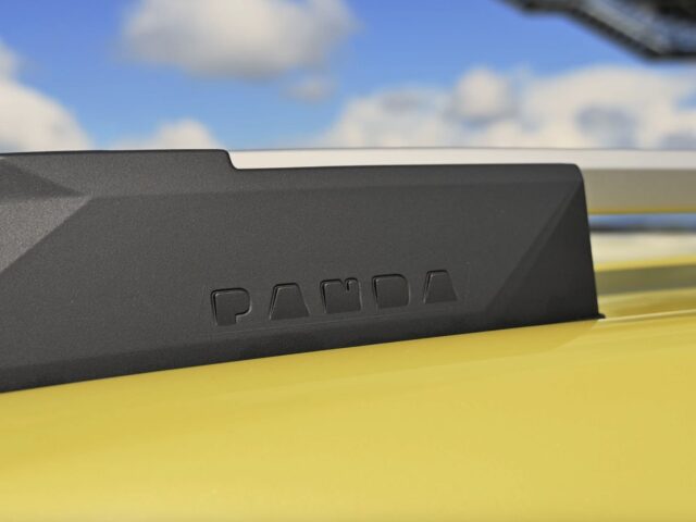 Close-up van een zwart 'Fiat Grande Panda'-logo in reliëf op de dakrail van een gele auto tegen een hemelachtergrond.