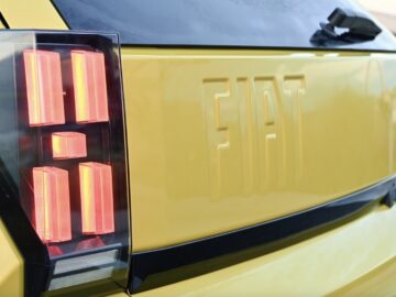 Close-up van de achterkant van een gele Fiat Grande Panda, met de nadruk op het verlichte achterlicht en het Fiat-logo in reliëf op de carrosserie van het voertuig.