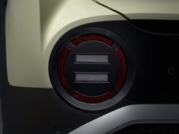 A close-up of the taillight of a Hyundai INSTER featuring a unique design with horizontal LED bars surrounded by red light. The car's body is a pale yellow color, adding to its bizarre specifications.