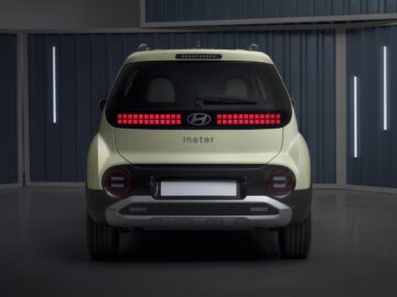 Achteraanzicht van een lichtgroene Hyundai INSTER-auto, met het opschrift 'Instier', tentoongesteld in een goed verlichte kamer met blauwe paneelwanden en verticale lichtstrips. Deze EV-prijspakker beschikt over werkelijk bizarre specificaties.