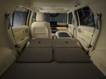 Inside view of the Hyundai INSTER SUV with beige leather seats and fold-down rear seats, with ample cargo space extending from the trunk to the front seats. At the front, a modern dashboard is visible, reflecting the appeal of the EV price point.