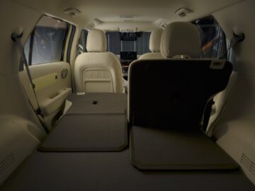 Intérieur d'un Hyundai INSTER montrant les sièges arrière, dont l'un est partiellement rabattu pour créer un espace de chargement supplémentaire, et les sièges avant avec le tableau de bord. Ce modèle au prix d'un véhicule électrique est doté de caractéristiques étonnantes qui allient fonctionnalité et technologie de pointe.