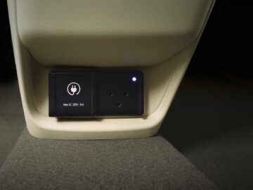 Eine Nahaufnahme des Innenraums eines Hyundai INSTER mit einer Steckdosenleiste, die eine Standard-Wechselstromsteckdose und eine Kontrollleuchte unter dem Armaturenbrett zeigt.