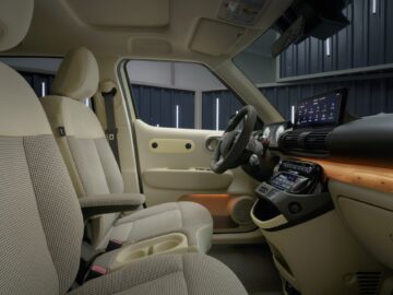 Binnenaanzicht van een moderne Hyundai INSTER met beige en zwarte stoelen, een touchscreendisplay op het dashboard en sfeerverlichting. Deze EV-prijspakker biedt zowel stijl als geavanceerde technologie voor een verbeterde rijervaring.