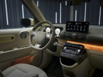 Intérieur d'une Hyundai INSTER moderne avec un volant à commandes, un tableau de bord numérique, un écran tactile central et des touches lumineuses sur les portes et le tableau de bord.