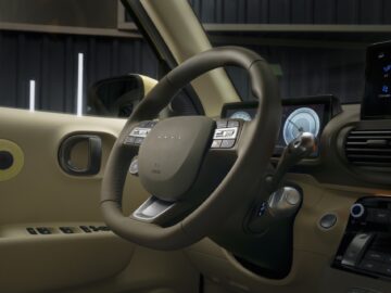 Un primer plano del interior de un Hyundai INSTER muestra el volante, el panel de instrumentos digital, el salpicadero y varios botones de control.