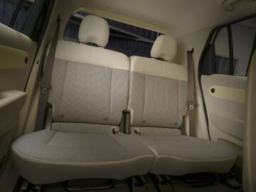 Der Innenraum des Hyundai INSTER, mit dem beigefarbenen Rücksitz mit Kopfstützen und Sicherheitsgurten. Es gibt keine Passagiere.
