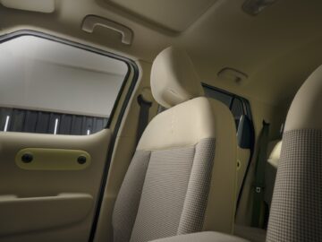 Interior of a Hyundai EV-priced car showing a close-up of the beige and gray upholstery of the front seats, with a window and part of the back seat visible in the background.