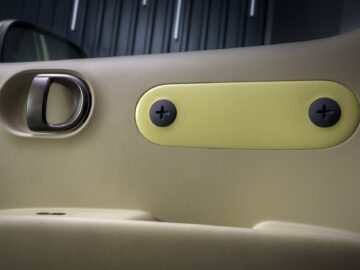 Interior view of a Hyundai INSTER car door with a metal door handle, a yellow panel with two black screw caps, and a side mirror visible through the window.