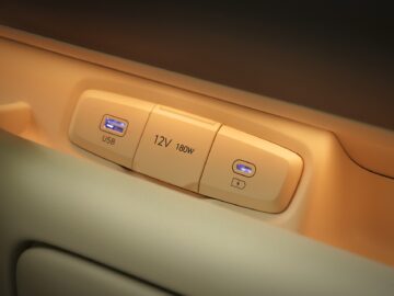 Nahaufnahme einer Steckdosenleiste in einem beigen Innenraum mit einer 12V-180W-Steckdose, einem USB-Anschluss und einem Knopf, der die bizarren Spezifikationen des Hyundai INSTER hervorhebt.