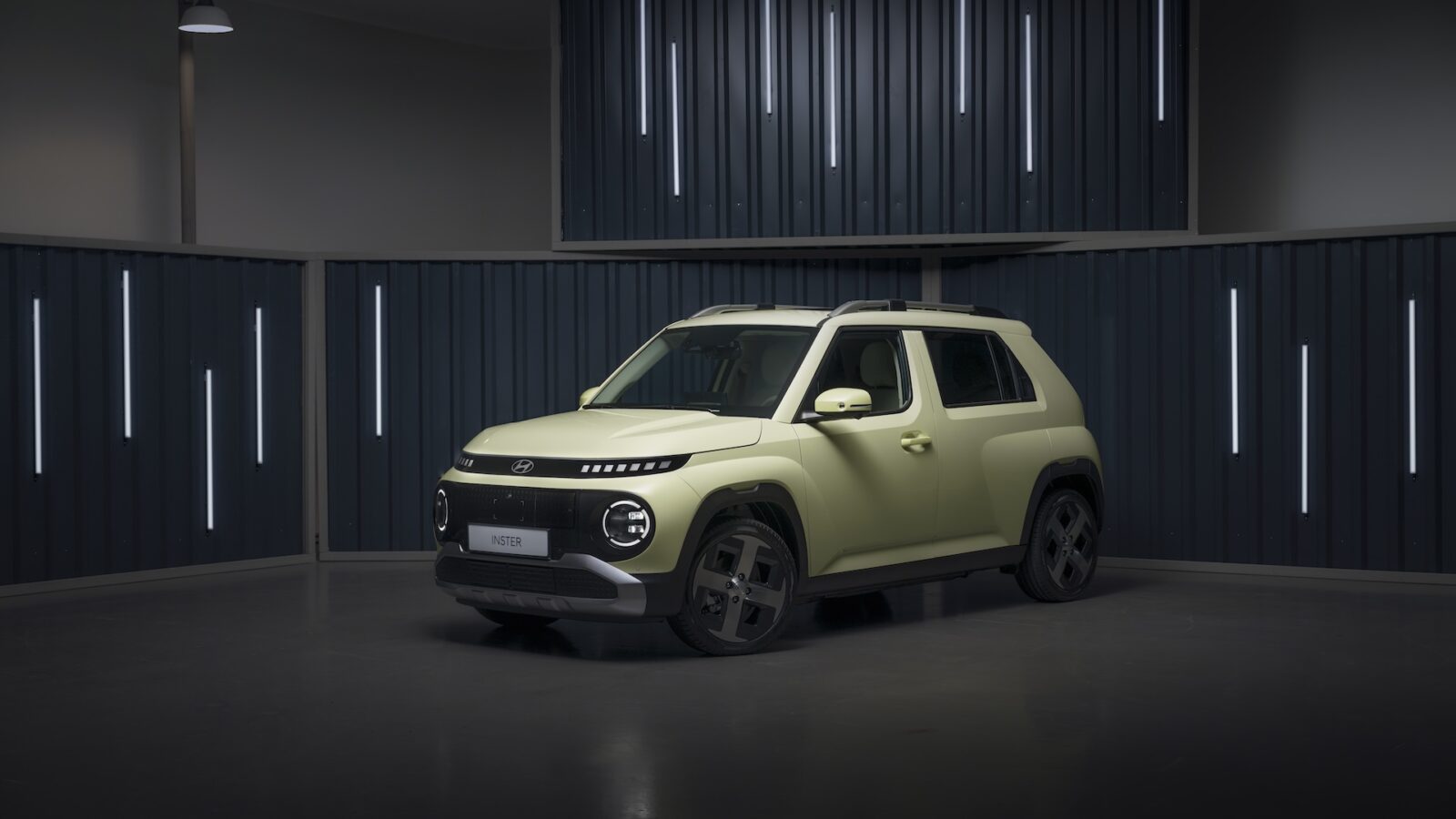 Een compacte, lichtgroene Hyundai SUV geparkeerd in een moderne, slecht verlichte studio met verticale lichtstrips op donkere muren.