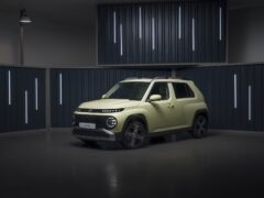 Een compacte, lichtgroene Hyundai SUV geparkeerd in een moderne, slecht verlichte studio met verticale lichtstrips op donkere muren.