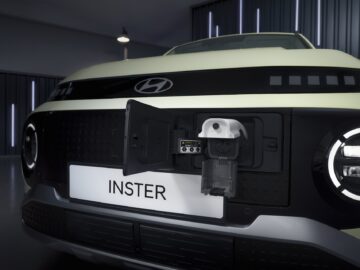 Close-up van een Hyundai INSTER met een oplaadpoort aan de voorkant geopend, waardoor een oplader voor elektrische voertuigen zichtbaar is. Op het kenteken staat 'INSTER'. Deze EV-prijspakker beschikt over indrukwekkende en bizarre specificaties die zeker de aandacht van elke liefhebber zullen trekken.