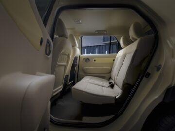 The interior of the Hyundai INSTER features beige, upholstered rear seats with a view of the front seats and car door. This modern design provides ample legroom and ensures comfort for all passengers.