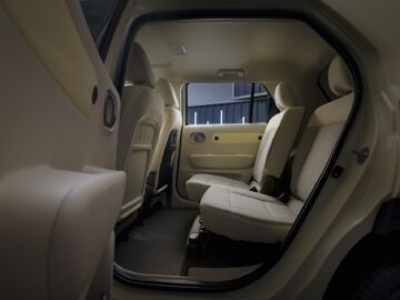 Inside view of the rear seat of the Hyundai INSTER, featuring beige upholstery and a spacious, minimalist design with open doors on both sides.