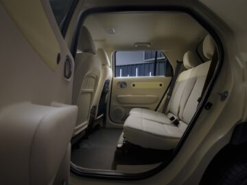 Inside view of the rear seat of a Hyundai INSTER through the open rear door, with beige upholstery, a row of headrests and a simple, modern design. The EV price point offers surprising comfort and elegance without outlandish specifications.