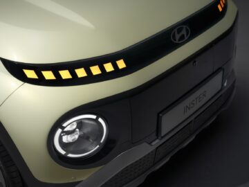 Nahaufnahme der Vorderseite eines Autos mit dem Hyundai INSTER-Logo, einem runden Scheinwerfer und einer Reihe von beleuchteten gelben Quadraten, die in den schwarzen Kühlergrill darüber integriert sind, mit bizarren Merkmalen.