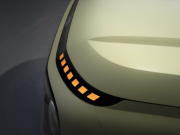 Close-up of the front of a Hyundai INSTER with a sleek, light green hood and a row of illuminated orange lights at the edge, showing off the unique EV price point.