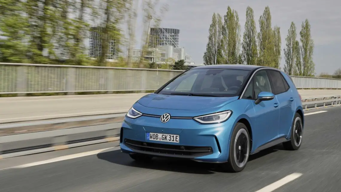 Een blauwe Volkswagen ID.3 elektrische auto met minder vermogen rijdt op een voorstedelijke weg, met bomen en gebouwen op de achtergrond, en toont trots zijn grotere prijskaartje.