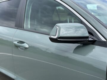 Close-up van de zijspiegel en de deurgreep van een auto op een glanzende, lichtgroene Kia Niro Electric die buiten geparkeerd staat.