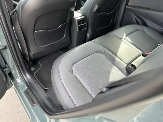 De afbeelding toont de achterbank van een Kia Niro Electric met grijze stoffen stoelen, waardoor een duidelijk zicht is op de vloermatten en de achterkant van de voorstoelen.