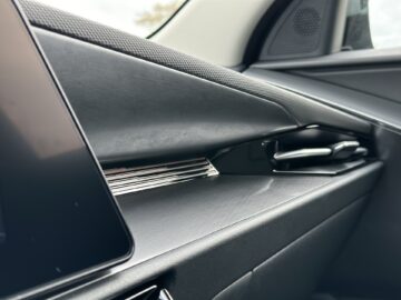 Close-up van het dashboard van een Kia Niro Electric, met een strak ontwerp met zwarte en metallic accenten. Aan de linkerrand van het beeld is een gedeelte van een scherm zichtbaar.