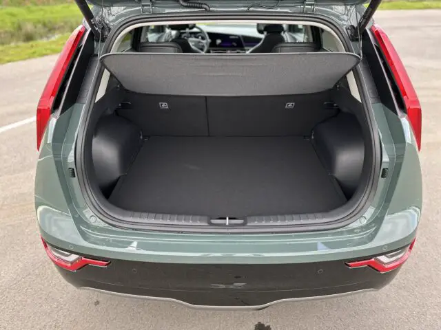 Afbeelding van de open kofferbak van een groene Kia Niro Electric met een ruime, lege bagageruimte met de achterbank omhoog.