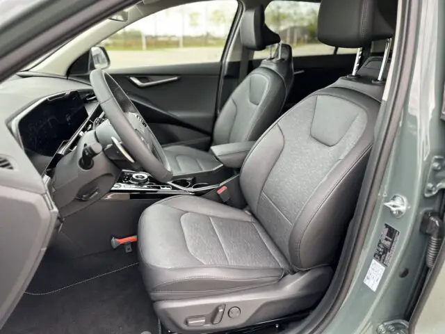 Binnenaanzicht van een Kia Niro Electric met de twee voorstoelen bekleed met grijze stof, een modern dashboard en een middenconsole met bekerhouders.