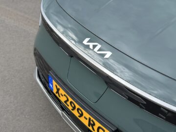 Close-up van de achterkant van een Kia Niro Electric, met het merklogo en een Europees kenteken met het nummer "X-299-RC". De auto staat geparkeerd op een grijs verhard oppervlak.