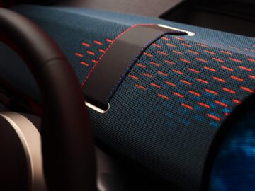 Close-up van een MINI Aceman-dashboard met een ontwerp van blauw en rood geruite stof en een zwarte leren band met ingewikkelde rode en blauwe stiksels. Deze elegante toets geeft stijl aan de innovatieve elektrische MINI en combineert traditie naadloos met moderniteit.