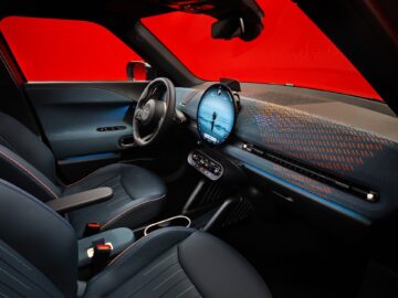 Binnenaanzicht van een moderne elektrische auto met een strak dashboard met een groot touchscreen-display en blauwe stoelen, die lijken op het verfijnde ontwerp van de elektrische MINI Aceman.