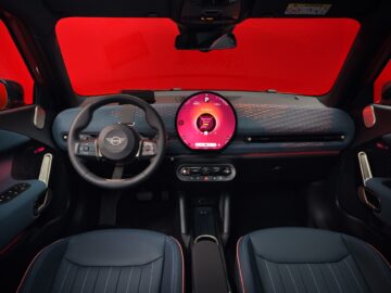 Interieur van een auto met een zwart en blauw dashboard, een rond infotainmentscherm met rode graphics, een zwart stuur met zilveren accenten en blauwe stoelen met rode stiksels. Deze opstelling is een voorbeeld van het moderne ontwerp dat te zien is in de elektrische MINI-modellen zoals de stijlvolle MINI Aceman.