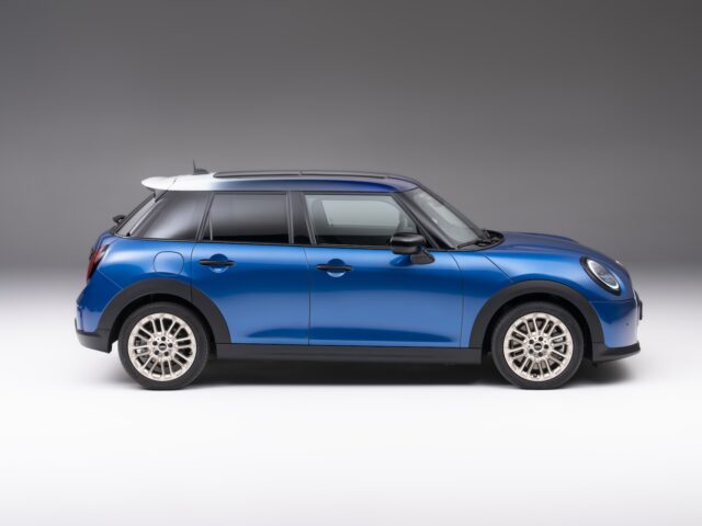 Zijaanzicht van een blauwe MINI Cooper 5-deurs met zilveren velgen, tegen een neutrale grijze achtergrond.