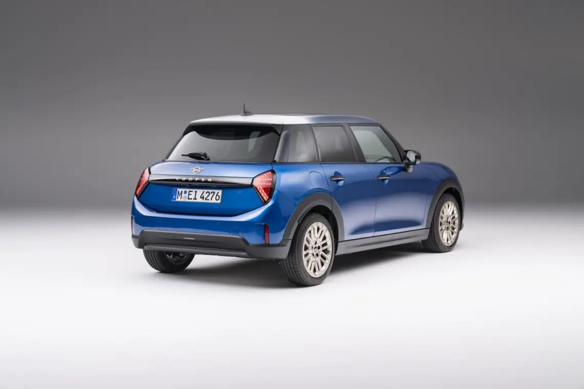 Een blauwe, moderne MINI Cooper hatchback met een Europees kenteken is linksachter afgebeeld op een effen witte achtergrond, wat het strakke 5-deurs ontwerp benadrukt.