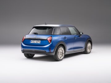 Een blauwe, moderne MINI Cooper hatchback met een Europees kenteken is linksachter afgebeeld op een effen witte achtergrond, wat het strakke 5-deurs ontwerp benadrukt.