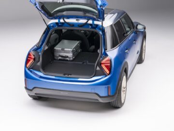 Een blauwe, nieuwe MINI Cooper SUV met 5 deuren en de achterklep open, onthult een gedeeltelijk beladen kofferbak met daarin een zilveren koffer.