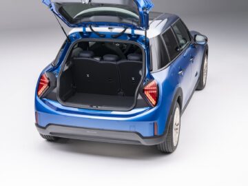 Een blauwe 5-deurs MINI Cooper met de achterklep open, waardoor een lege laadruimte en achterovergeklapte stoelen zichtbaar zijn, in een studiosetting.