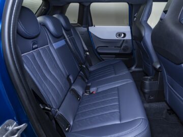 De afbeelding toont het interieur van de achterbank van een nieuwe 5-deurs MINI Cooper met blauw lederen bekleding, voorzien van twee hoofdsteunen, veiligheidsgordels en een middenconsole. De linkerdeur is zichtbaar.