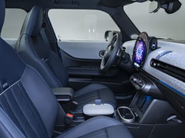 Interieur van een moderne 5-deurs met blauwleren stoelen, een digitaal touchscreen-display op het dashboard en verschillende bedieningsknoppen en compartimenten die lijken op het stijlvolle ontwerp van een MINI Cooper.