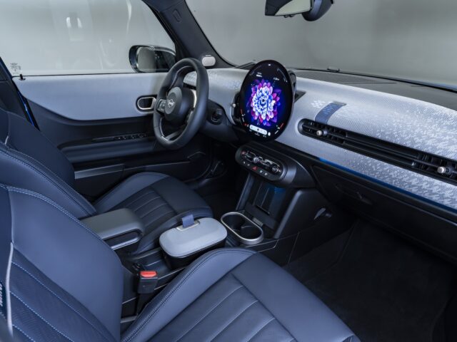 Interieur van een nieuwe MINI Cooper met zwart lederen stoelen, een rond touchscreen display op het dashboard en een compacte middenconsole met bekerhouders. Het stuur is bij dit stijlvolle 5-deursmodel voorzien van geïntegreerde bedieningselementen.