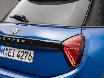 Close-up van de achterkant van een nieuwe blauwe MINI Cooper S 5-deurs. Kentekenplaatnummer "M EI 4276" is zichtbaar, samen met een opvallend achterlichtontwerp en het iconische Mini-logo.