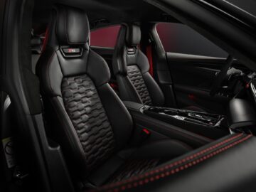 Het interieur van de Audi RS e-tron GT is voorzien van zwartleren stoelen met rode stiksels, RS-logo op de hoofdsteunen en een middenconsole met moderne bedieningselementen. Deze auto beschikt over 1.000 pk en biedt een ongeëvenaarde prestatie-ervaring.