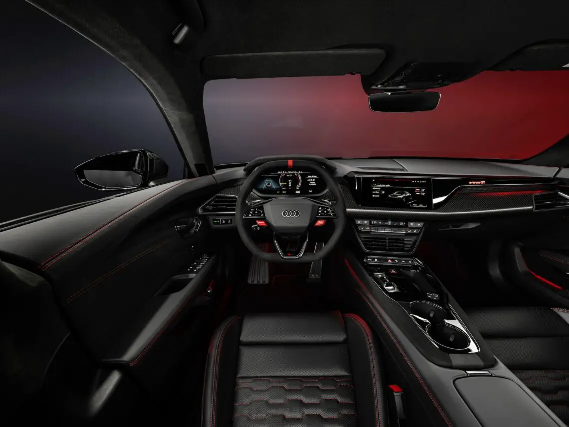 Interieur van de Audi RS e-tron GT met een digitaal instrumentenpaneel, stuur en dashboard met verschillende bedieningselementen en schermen, met zwarte en rode accenten die verwijzen naar het krachtige karakter ervan.