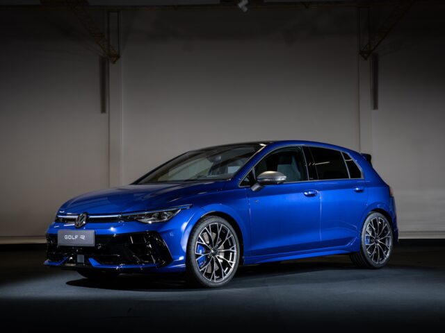 A blue Volkswagen Golf R hatchback, with its sleek design and alloy wheels, is on display in a dimly lit room, celebrating 50 years of sporting excellence.