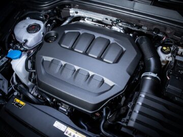 A clean and modern car engine bay of a sporty Volkswagen Golf with a large black hood, visible coolant reservoir and various engine parts celebrating 50 years of innovation.