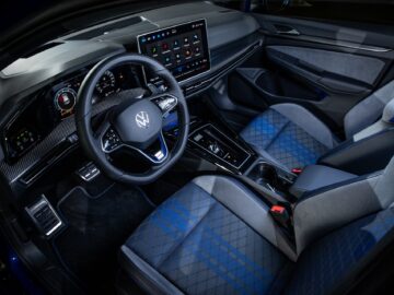 Interior of a modern Volkswagen Golf with a logo on the steering wheel, touchscreen display, digital dashboard and sport seats with blue and gray accents. The control buttons add to the sporty design.