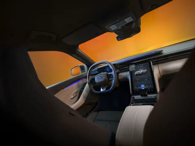 Futuristisch auto-interieur met een stuur met het iconische Ford-logo, een groot centraal touchscreen-display en een modern dashboardontwerp, geïnspireerd op de tijdloze elegantie van de Ford Capri, vanuit het perspectief van de bestuurdersstoel.